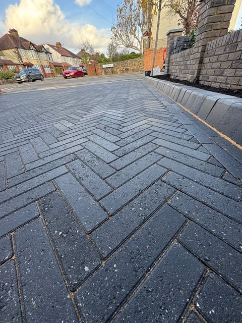 Newly paved residential driveway with herringbone pattern paving stones in a suburban street with brick homes