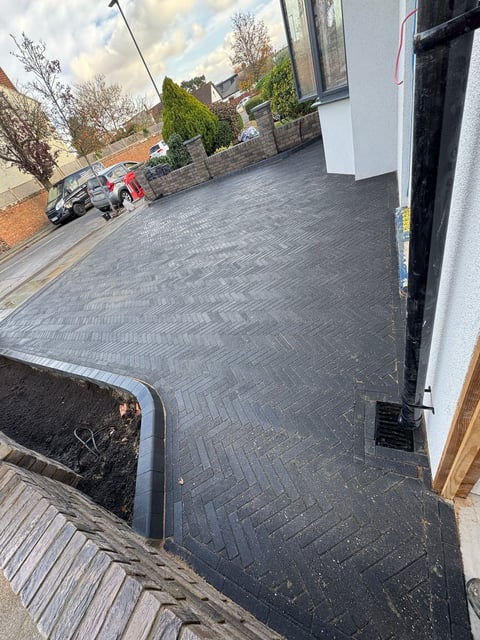 Newly installed dark herringbone paved driveway in front of a residential property with white wall and black door