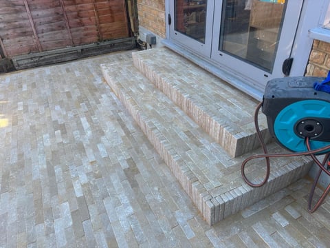 Patio with herringbone brick flooring, stepped seating area, white doors, and blue pressure washer equipment on the right