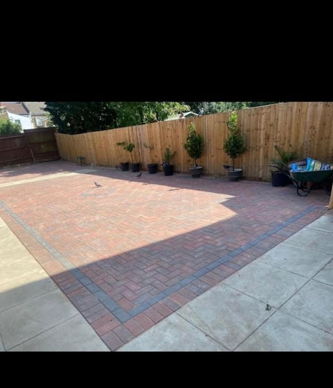 Backyard patio with red brick and gray pavers, wooden fence, potted plants, wheelbarrow, and concrete edge border