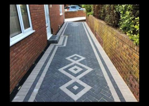 Narrow brick pathway with decorative paving pattern featuring diamond shapes in gray and white between red brick walls