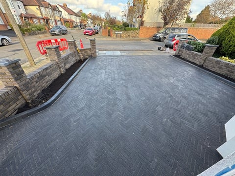 Newly paved driveway with herringbone pattern asphalt in a residential street with parked cars and brick buildings